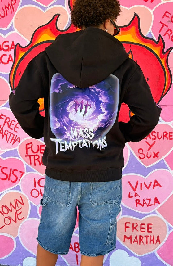Person wearing a black hoodie with a colorful design on the back, standing in front of a mural with political text.